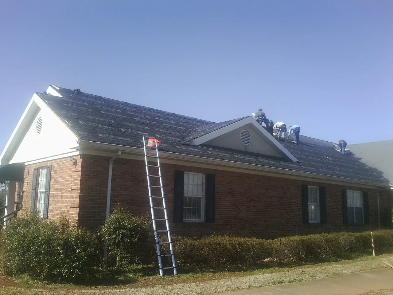 Crew tearing shingles off a brick ranch roof with a ladder set — Emergency Roof Repair work by our crew in Defuniak Springs
