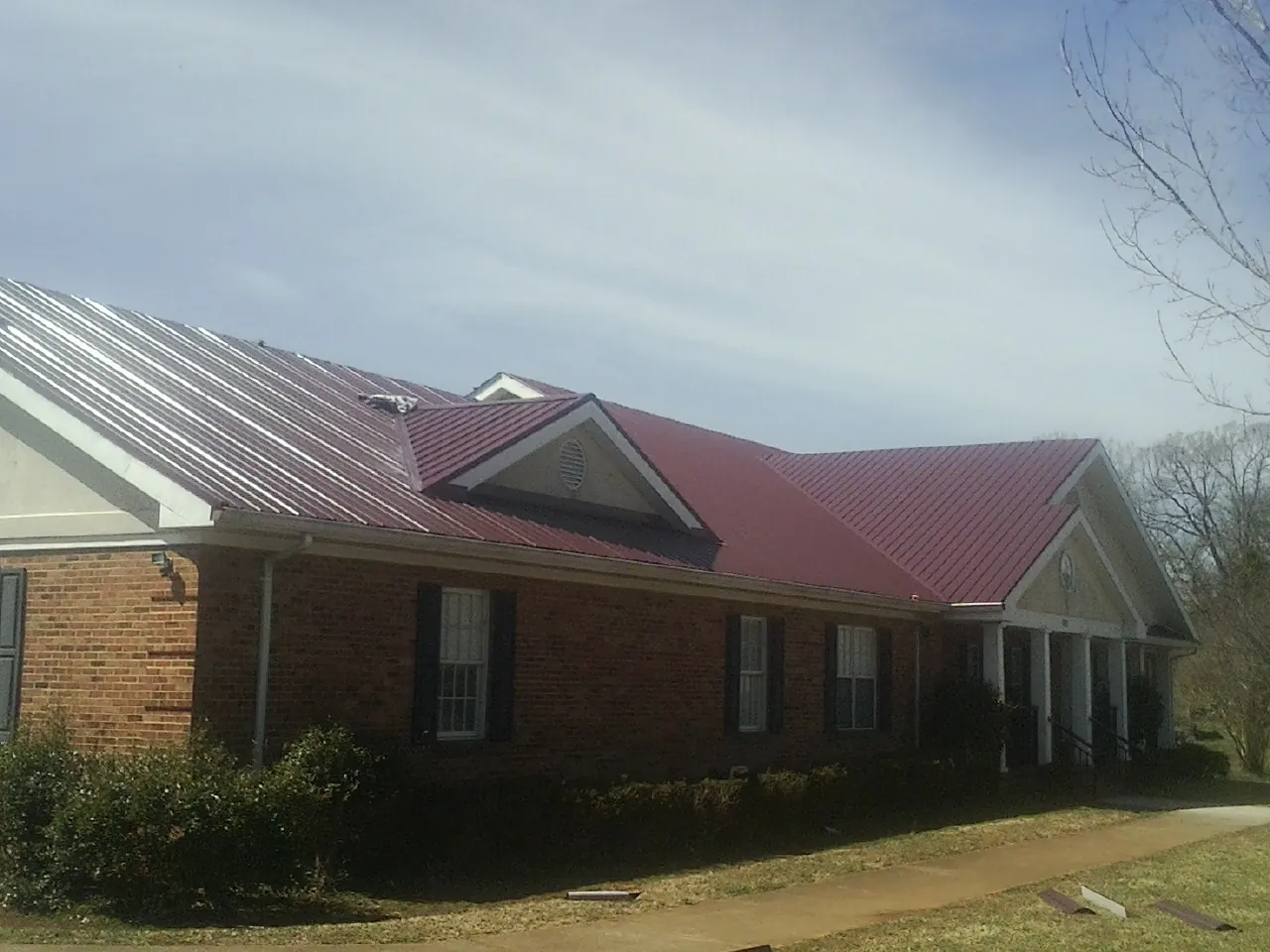 Red metal roof with gabled entries on a long brick building, from a Hail Damage Roof Repair job in Defuniak Springs