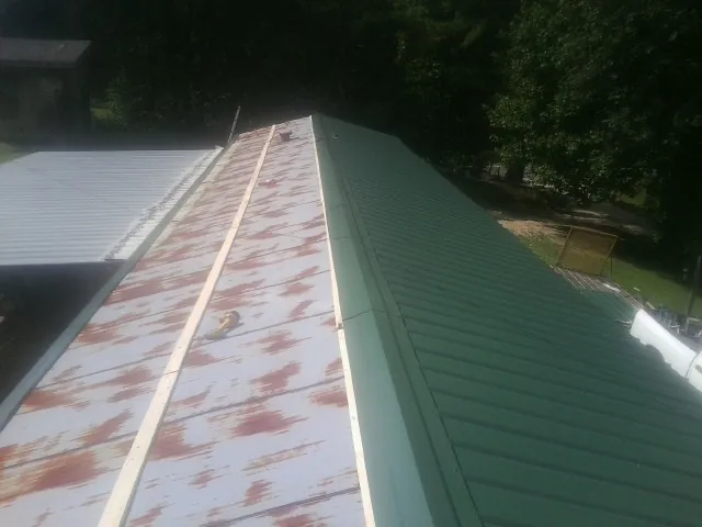 Old rusted panels beside newly installed green metal roofing — Wind Damage Roof Repair by Roofing Brothers in Defuniak Springs