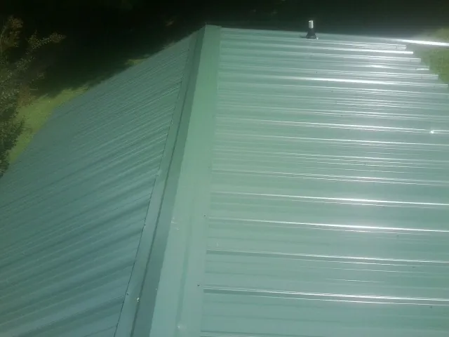 New green metal panels meeting at the ridge of a roof — Flat Roof Repair work by our crew in Defuniak Springs