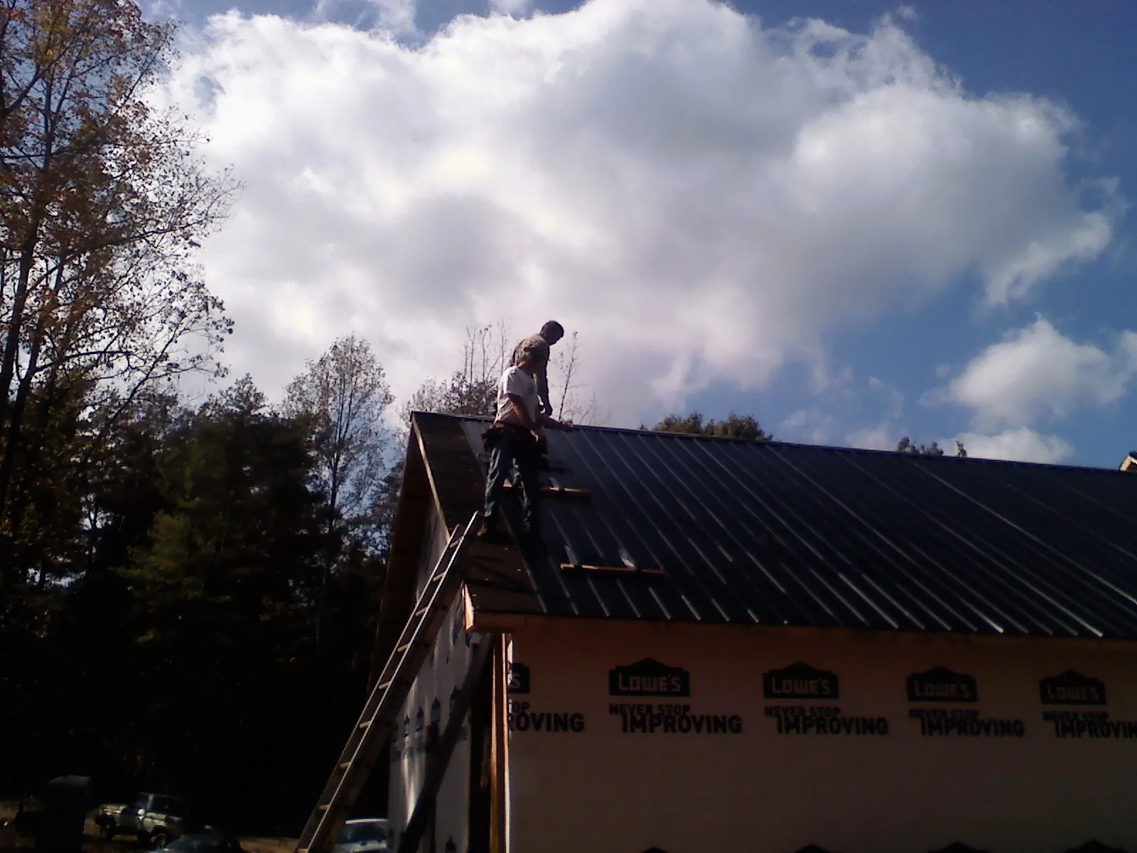 Roofer fastening dark metal panels high against a cloudy sky, from a Roof Inspection job in Defuniak Springs