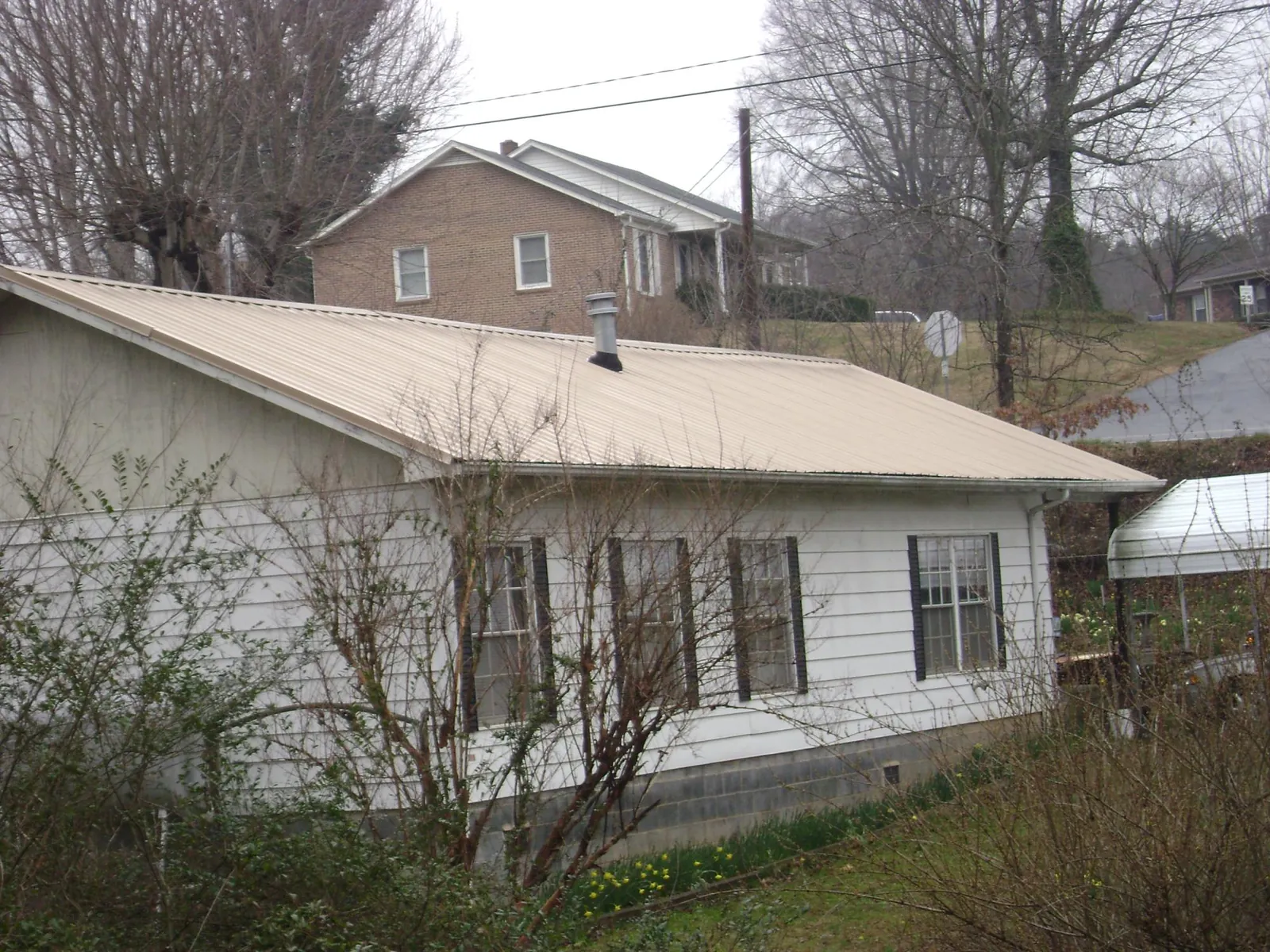 Tan metal roof on a white sided house set into a hillside — Commercial Roofing by Roofing Brothers in Defuniak Springs