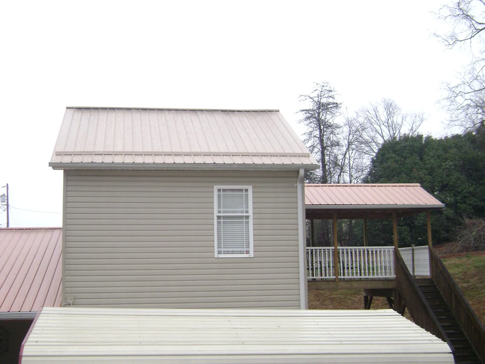 Tan metal roofs on a two story addition and attached porch, from a Roof Replacement job in Defuniak Springs